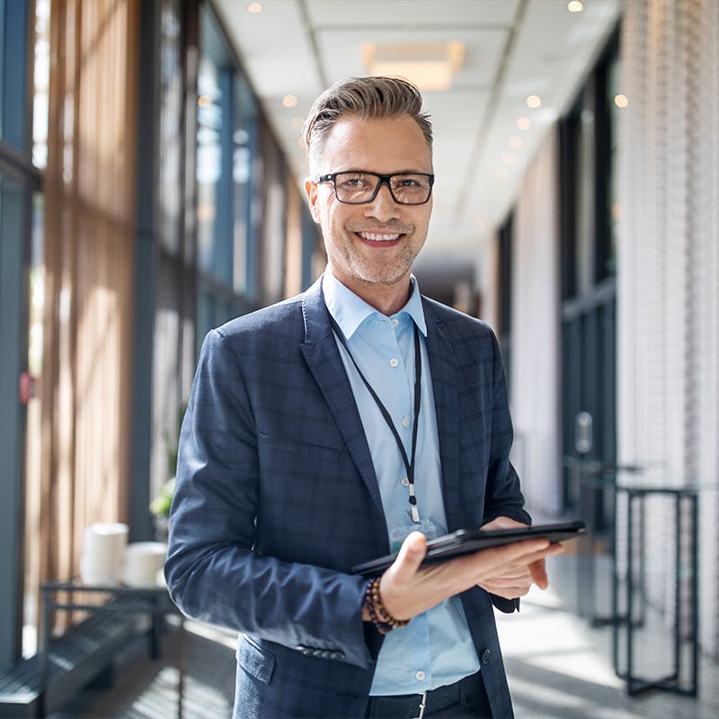 Portrait of smiling mature businessman standing outside auditorium with a digital tablet.