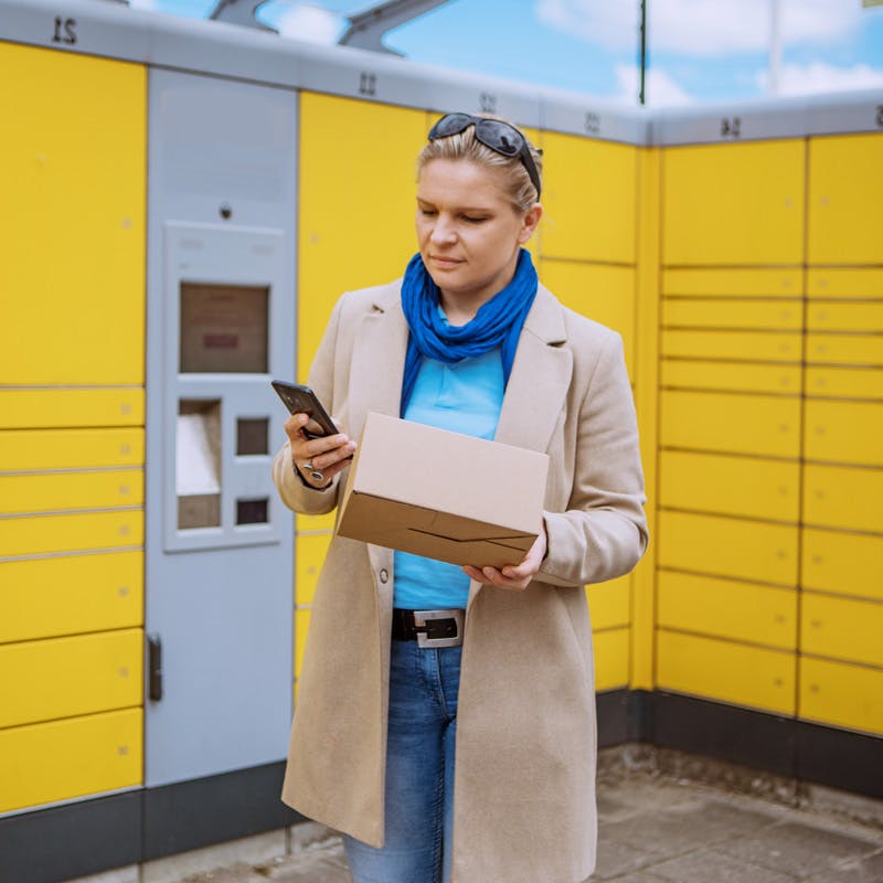 Woman holding a package while looking at her phone with intelligent lockers in the background