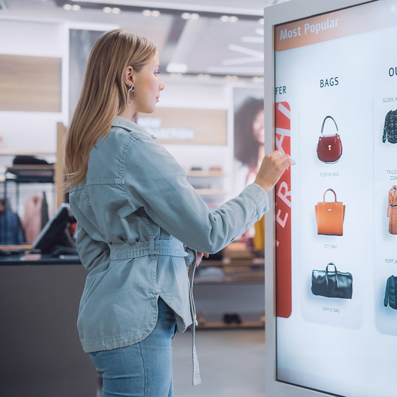 Woman using an in store touch screen kiosk to look at hanbag options