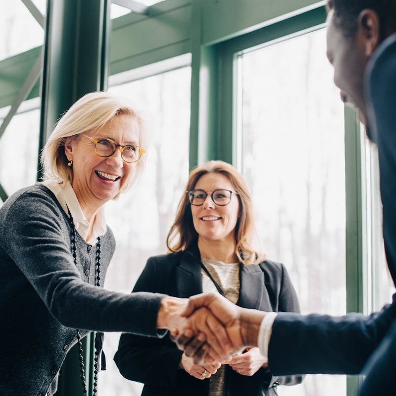 Two woman smiling while one of them shakes the hand of a business man
