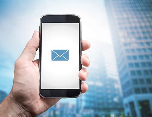 Man holding phone with email icon with building in background