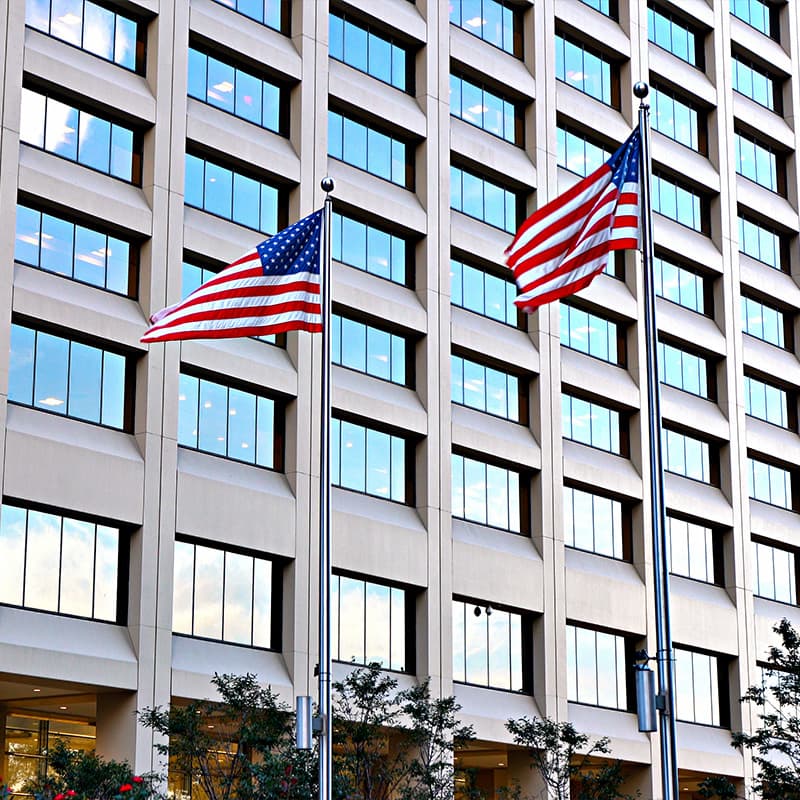 Two US flags on flagpoles swaying in the wind in front of a government building